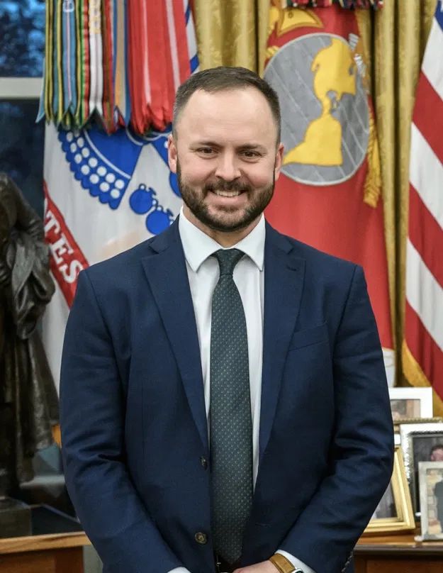 Jay Fields in the Oval Office, standing before the presidential flags.